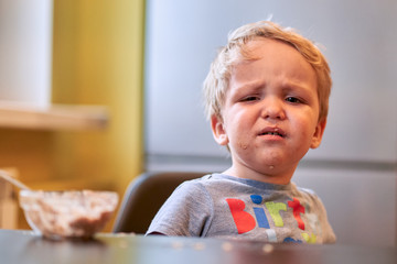 two-year-old boy is naughty and does not want to eat porrige with a spoon at the table in the...