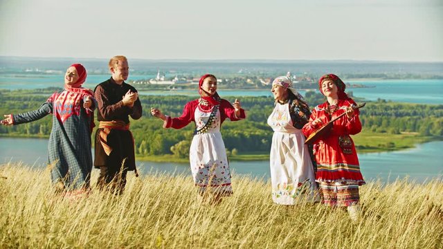 Young ensemble in traditional russian clothes dancing on the field by the music