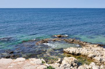 View of the sea from the rocky shore. Blue-turquoise water, open space and a vessel in the road away.