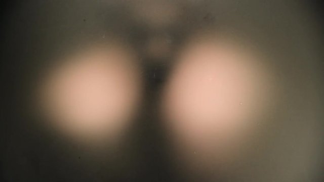 Unrecognizable scary and naked man looking behind a frozen glass carefully.