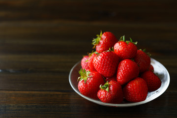 Freshly picked organic strawberries in a glass bowl. Dark wooden table, water, high resolution