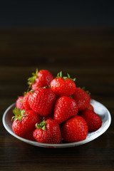 Freshly picked organic strawberries in a glass bowl. Dark wooden table, water, high resolution