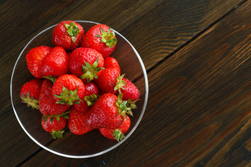 Freshly picked organic strawberries in a glass bowl. Dark wooden table, water, high resolution