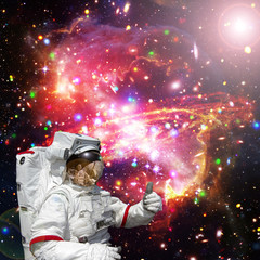 Astronaut gives thumbs-up against outer space, galaxies and stars. The elements of this image...