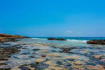  black and yellow rocks and stones and blue sea on the shore of Ayia Napa, Cyprus