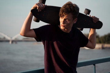 Closeup shot of handsome teenager posing with longboard at sunset 