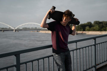 Beautiful teenager posing with long board at sunset on bridge 