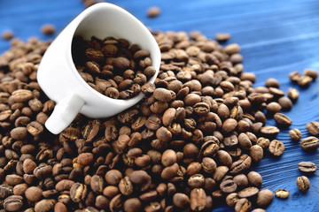 white cup in coffee beans lying on a blue wooden background