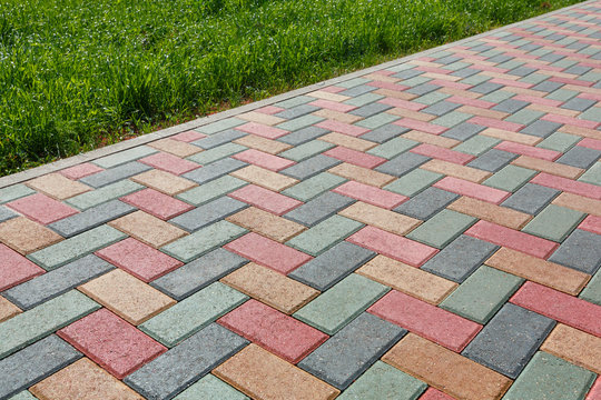 Colorful cobblestone road pavement and lawn divided by a concrete curb.