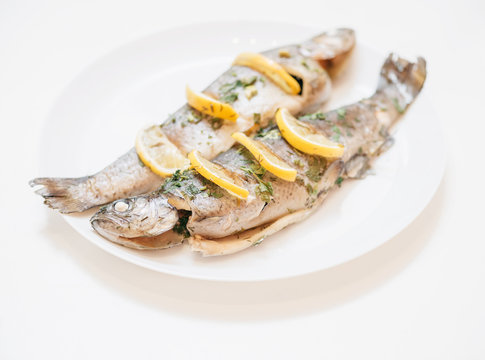 Two baked fish trout dish with lemons on a white plate.