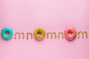 "Om nom nom" quote made of sprinkles and colorful donuts on pink background. 