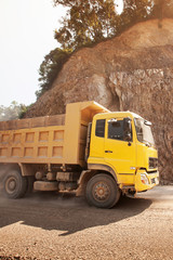 Fototapeta na wymiar A yellow dump truck driving on a dusty mountain road.