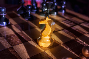 One white knight staying against full set of black chess pieces. Closeup of chessboard with wooden pieces on table in sunlight, game of lights. Business concept success & strategy