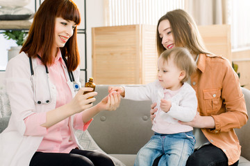 Young woman pediatrician prescribes and gives a medicine to ill baby girl, sitting with her mother