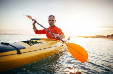 Active senior man paddling the kayak on a sunset sea