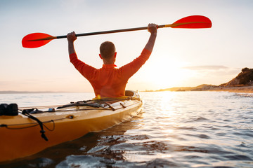 Rear view of active senior man holds kayak paddles high