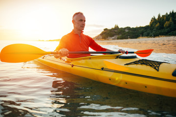 Active senior in a kayak enjoy sunset sea.