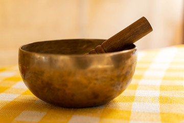 Singing bowl with stick on a yellow tablecloth