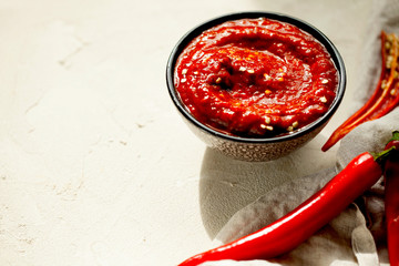Traditional homemade rose harissa-hot chili pepper sauce paste with garlic and olive oil in small bowl on white plaster background with copy space for text.Tunisia and Arabic cuisine adjika