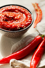 Traditional homemade rose harissa-maghrebi red hot chiles paste with garlic and olive oil in small bowl on white plaster background close-up.Tunisia and Arabic cuisine adjika.Vertical orientation