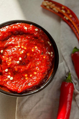 Traditional homemade rose harissa-hot chili pepper sauce paste with garlic and olive oil in small bowl on white plaster background close-up top view.Tunisia and Arabic cuisine adjika