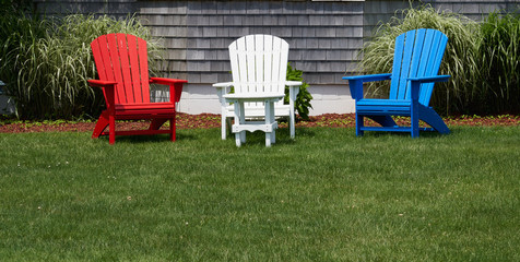 red white and blue wooden adirondack chairs on a green lawn in front of a house
