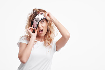 Sleepless night. Stressed and tired caucasian girl in eyemask and white pajamas standing on white...
