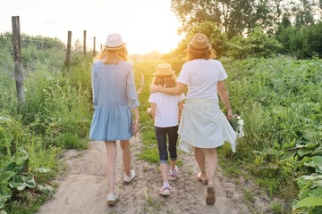 Mother with children two daughters walking along a country road, back view