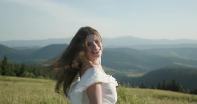 Attractive woman on a mountain peak with her long hair blowing in the wind smiling and trying to keep her hair off her face
