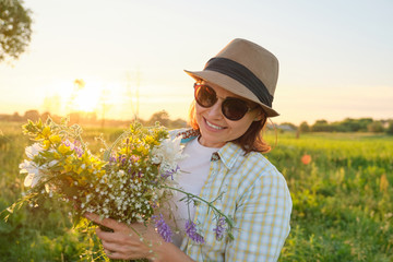 Mature woman with flowers in a summer meadow, golden hour