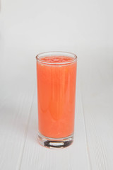 A thin, high transparent glass is filled with freshly prepared citrus juice which stands on an isolated wooden background of white color.