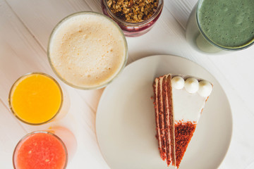 a red velvet cake on the background of glasses with various colored drinks (juice, coffee, smoothie, milkshake) standing on a white wooden table. A concept for a baker's dessert, a cafe, a restaurant