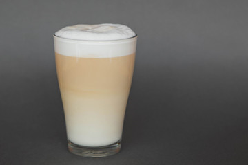 A large transparent glass filled with Latte cooked in a third wave coffee shop is photographed on a gray, isolated background, photo for the menu