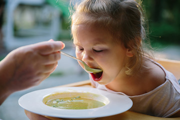 Child feading with soup at the restaurant garden