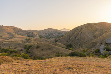 Hilly and mountainous steppe under the rays of the early sun with yellowed dry grass
