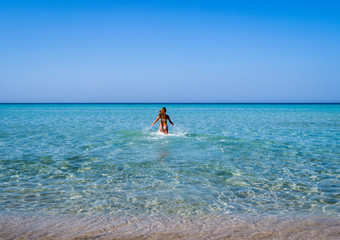Fototapeta na wymiar Slim and athletic girl in a colourful bikini having fun on a wonderful beach with crystal clear water -vacation-fitness-wellness