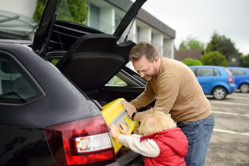 Handsome man and his little son going to vacations, loading their suitcase in car trunk. Automobile trip in the countryside. Roadtrip for family with kids