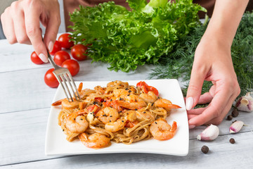 Hands young woman with plate of tasty pasta with shrimp.