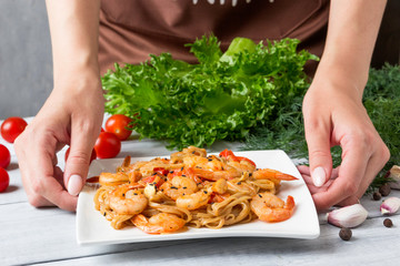 Hands young woman with plate of tasty pasta with shrimp.