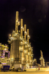 Photo of metal structures on the large oil and gas processing plant. Night photo of pipes and metal constructions at an oil or gas field plant. Construction of an oil refinery.