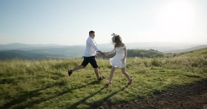 Love in the mountains. Man and woman run along the road to the horizon somewhere on the hill while sun shines over them
