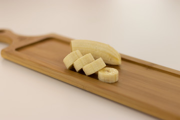 A beautifully sliced banana lies on a wooden board against a white background