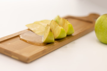 A beautifully sliced an apple poured with honey is lying on a wooden board on a white background