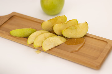 A beautifully sliced an apple poured with honey is lying on a wooden board on a white background