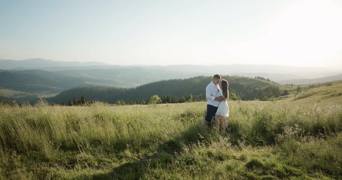 Young adorable couple embracing, kissing each other in the green dense mountain region. Summertime, sunset. Couple goals. Forever in love. Love story