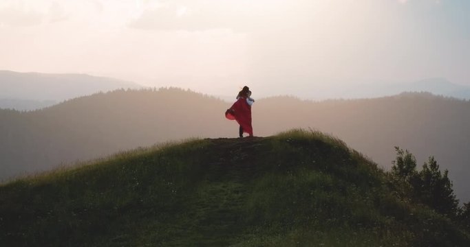 Young couple in love enjoying a sunset over the mountains. Amazing l view of young adorable couple embracing, kissing each other in the green dense mountain region. Summertime, sunset. Forever in love