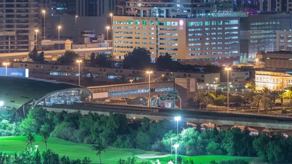 Metro station services both the Dubai Internet City and Dubai Media City districts of Dubai, as well as Golf Club night timelapse. Aerial view from Greens district with illuminated buildings on a