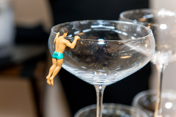 Champange glass decorated with male figurine clad in speedo swimsuit while climbing over rim.