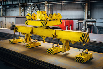 Overhead crane with magnetic grippers lifting steel sheets