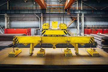 Overhead crane with magnetic grippers lifting steel sheets